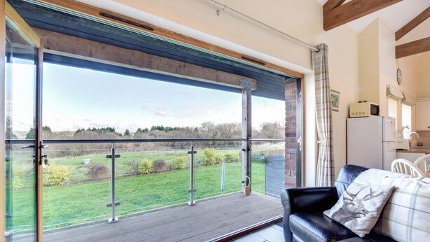 Ein Balkon mit Blick auf ein grünes Feld, ein schwarzes Ledersofa und eine Küchenzeile mit einem Kühlschrank.