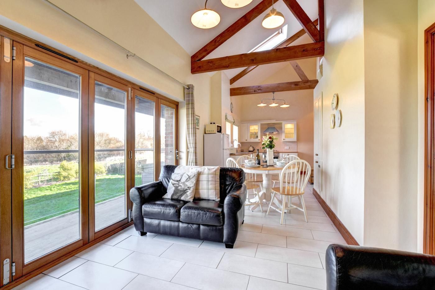 A spacious living area with a black leather sofa, a dining table with chairs, and a kitchen in the background.