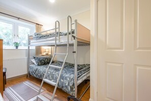Dormitorio con literas, ventana, radiador, lámpara y planta.