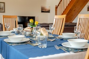 Mesa de comedor servida con platos, tazones, vasos y pan blancos, con un mantel azul.