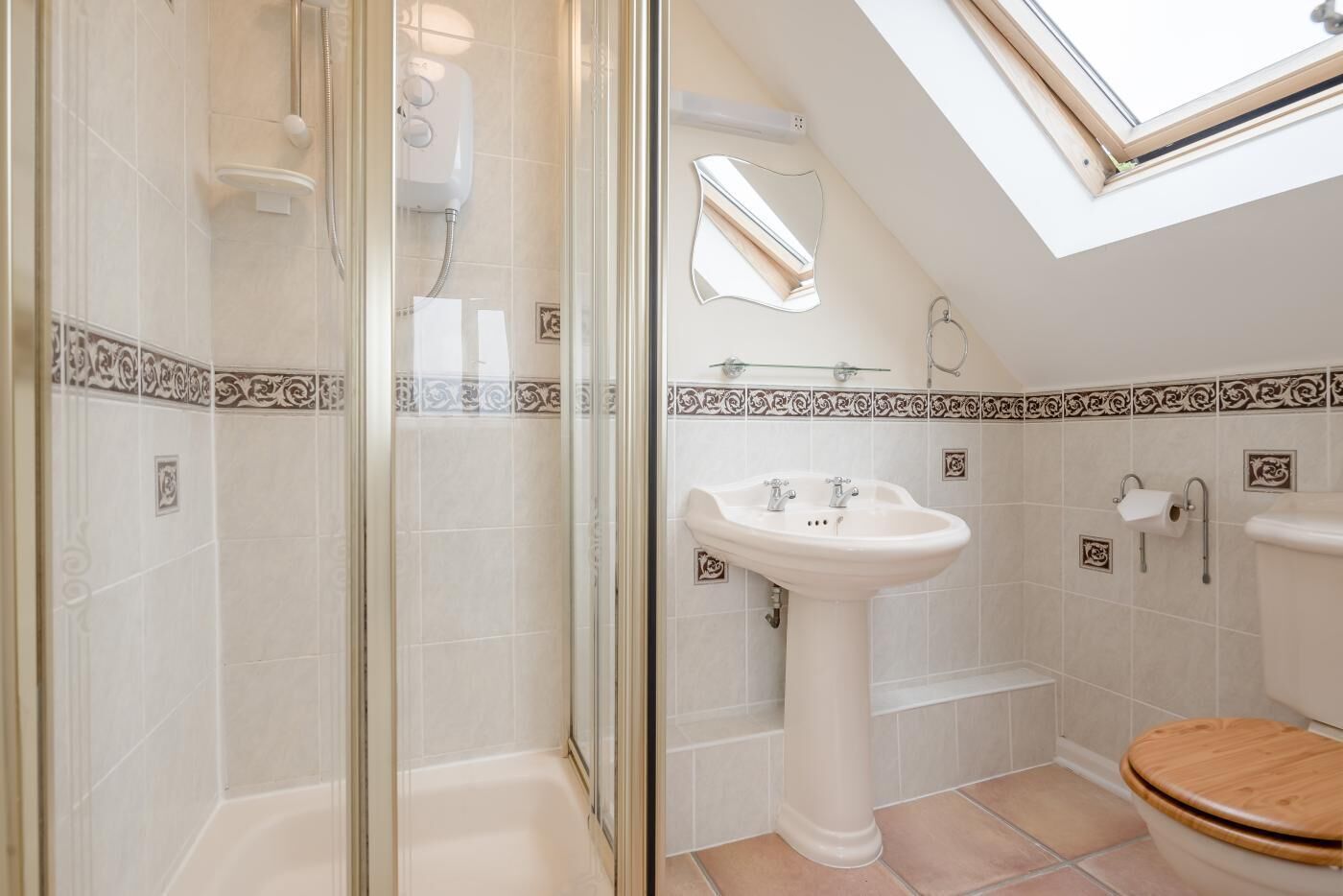 A bathroom with a glass shower enclosure, a pedestal sink, and a toilet with a wooden seat.