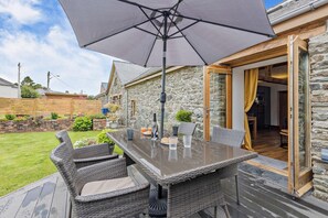 An outdoor dining area with a table and chairs, a large umbrella, and a stone building with a wooden deck. - 2 Bed in Bala (oc-82212) (Bala)