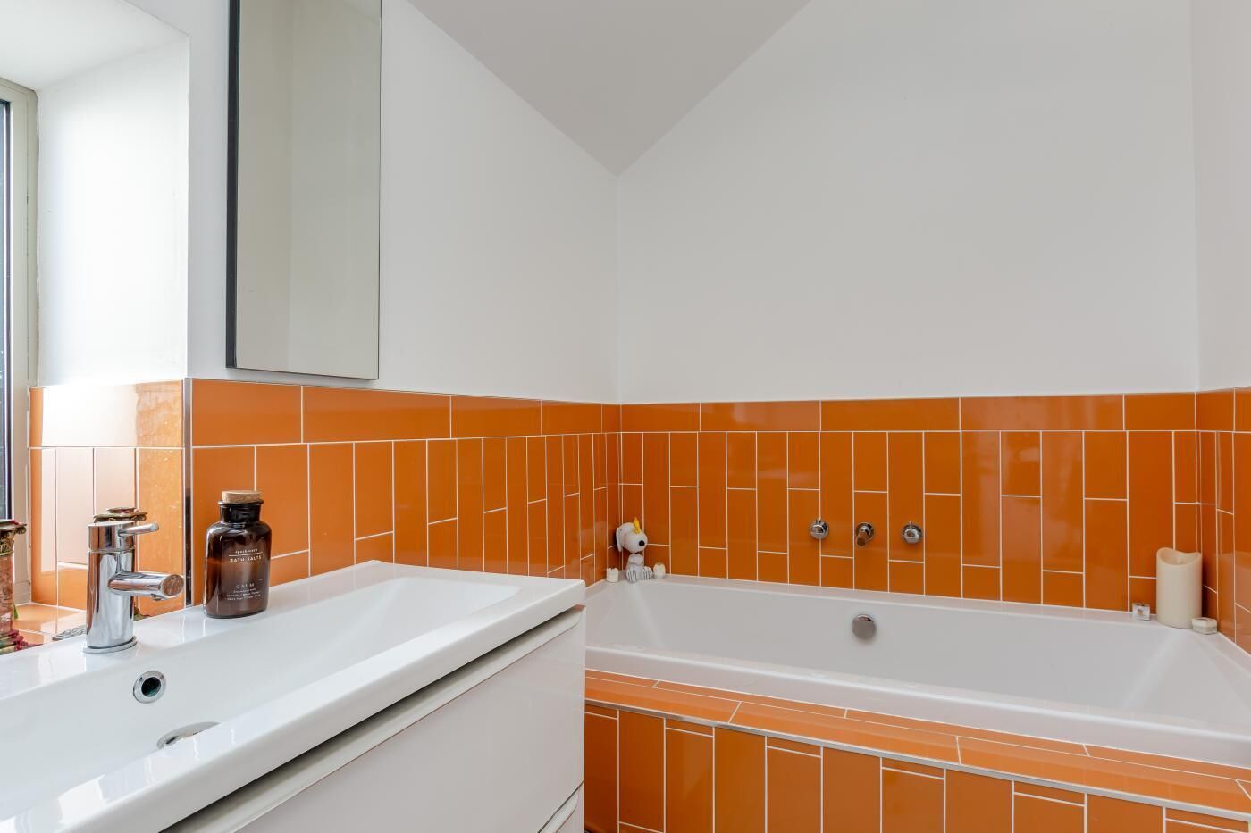 Ein Badezimmer mit weißem Waschbecken, einer Badewanne und orangefarben gefliesten Wänden.