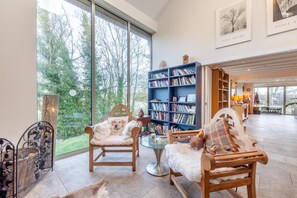 Ein geräumiges Wohnzimmer mit großen Fenstern, einem Bücherregal und zwei Sesseln.