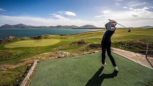 Un parcours de golf offrant une vue sur la mer et les montagnes en arrière-plan.