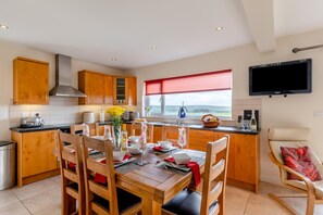 A modern kitchen with wooden cabinets, a dining table set for four, and a view of the sea through a window.