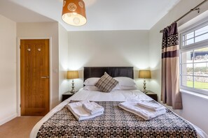 A neatly made bed with a patterned bedspread, two bedside lamps, a wooden door, and a window with curtains.