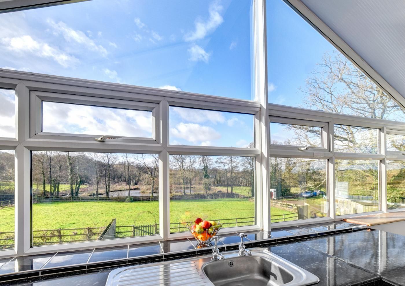 A kitchen with a large window overlooking a green landscape.