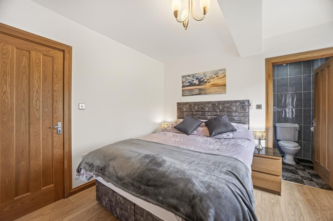 A bedroom with a bed, bedside table, nightstand, and a view of the bathroom.