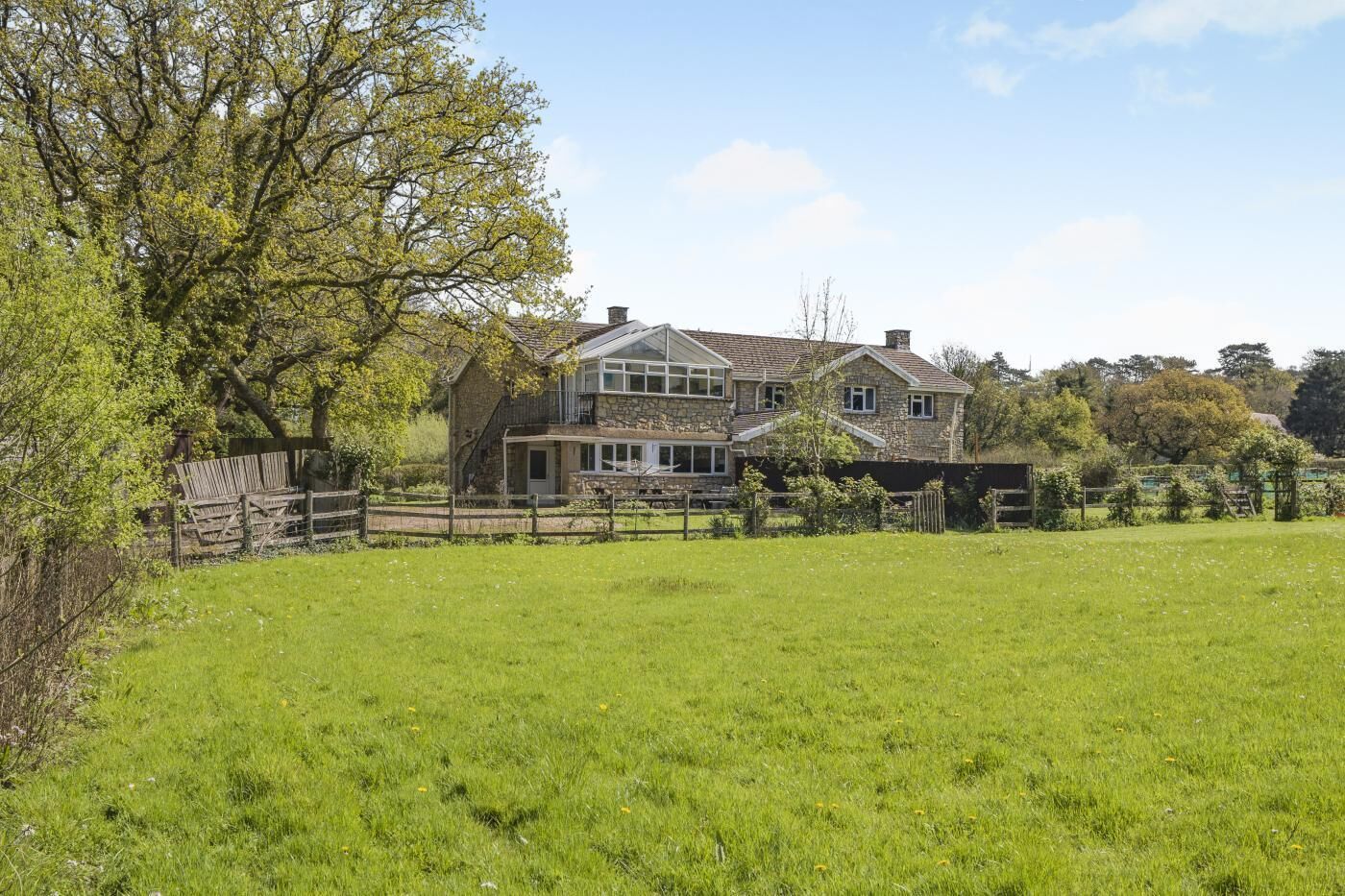 A two-story stone house with a large front lawn and a wooden fence.