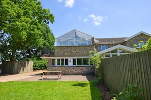 A two-story stone house with a large tree in the yard, a wooden fence, and a bench. - 2 Bed in Cardiff (oc-45394) (Peterston-super-Ely)