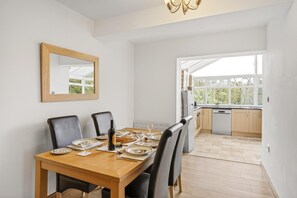 Een eetruimte met een houten tafel gedekt voor vier personen, een spiegel aan de muur en uitzicht op de keuken.