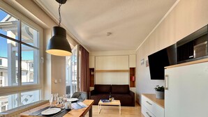 A compact hotel room with a dining table, a sofa, a small TV, and a kitchenette. - Perfekt fur 2 - Moderne Ferienwohnung Strandnah in Sellin (Sellin)