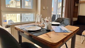 A dining table set with plates, cutlery, and a pitcher, with a view of buildings through a window. - Perfekt fur 2 - Moderne Ferienwohnung Strandnah in Sellin (Sellin)
