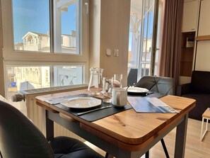 A dining table set with plates, cutlery, and a pitcher, with a view of buildings through a window. - Perfekt fur 2 - Moderne Ferienwohnung Strandnah in Sellin (Sellin)
