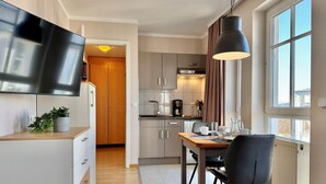 A modern kitchen with a dining area, wooden cabinets, a flat-screen TV, and a large window. - Perfekt fur 2 - Moderne Ferienwohnung Strandnah in Sellin (Sellin)