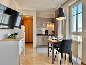 A modern kitchen with a dining area, wooden cabinets, a flat-screen TV, and a large window. - Perfekt fur 2 - Moderne Ferienwohnung Strandnah in Sellin (Sellin)