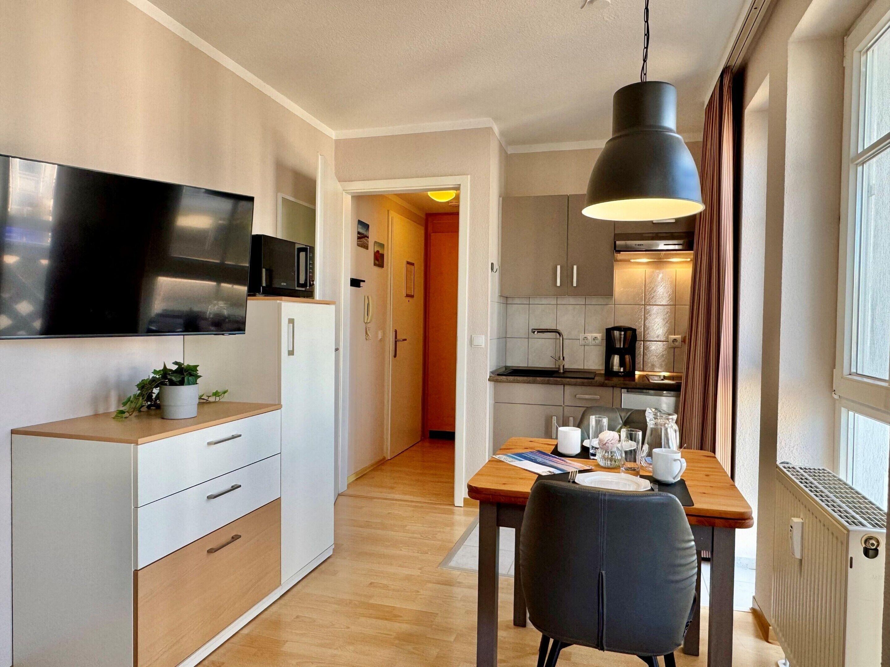 Uma cozinha moderna com televisão de tela plana, uma mesa de jantar com cadeiras e uma luminária pendente.