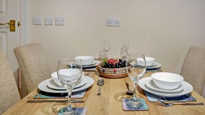 Una mesa de comedor dispuesta con platos, tazones, copas de vino y una cesta de uvas.