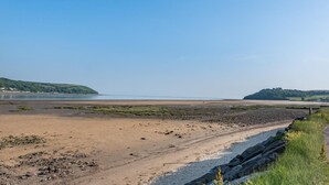 Un paisaje costero con una playa arenosa, costa rocosa y colinas al lejano.