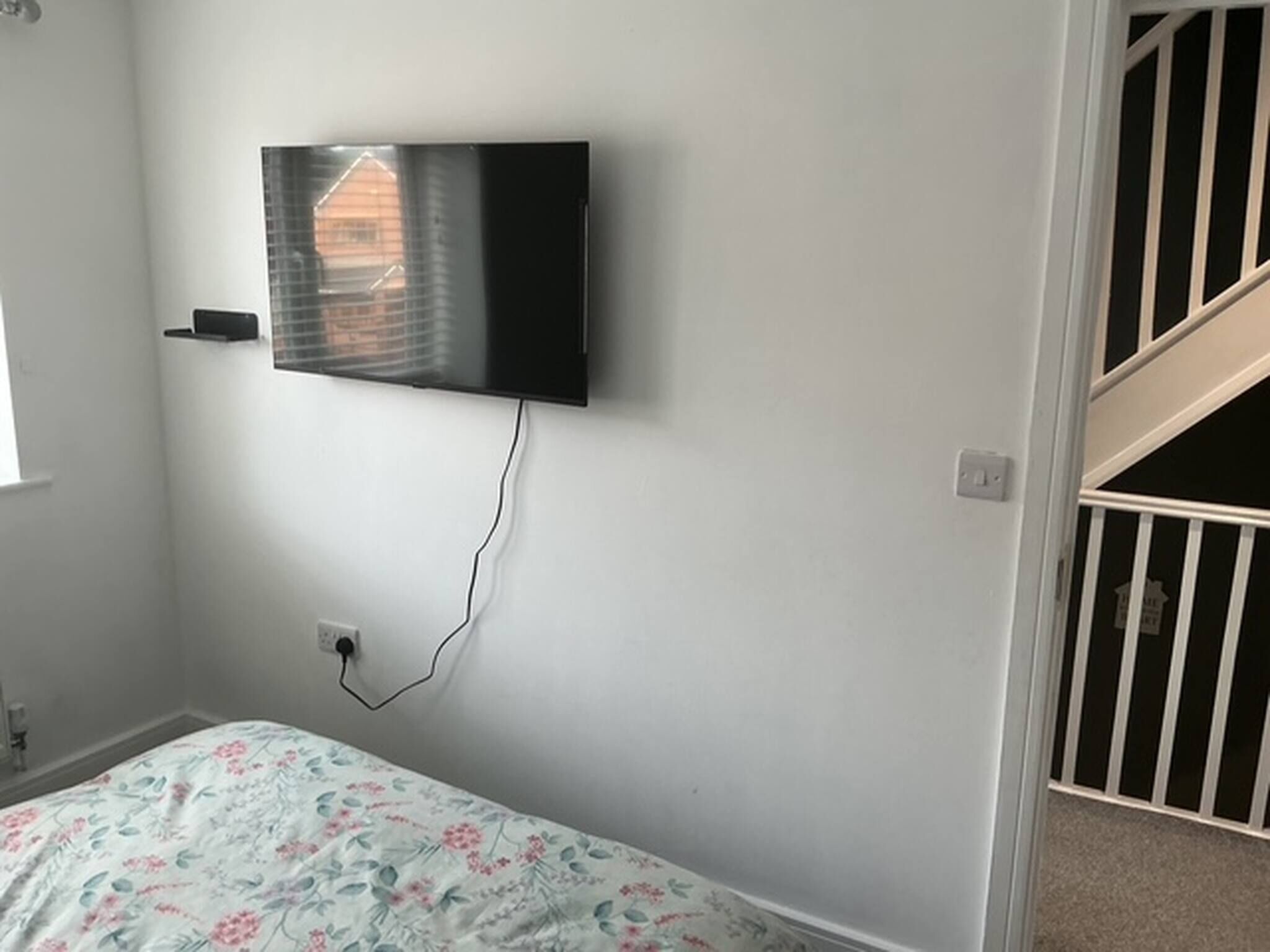 Een slaapkamer met een bed, een aan de muur bevestigde televisie en een trap.