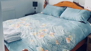 Een slaapkamer met een bed, nachtkastje, lamp, raam en spiegel.