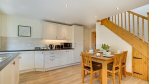 Una cocina con armarios blancos, una mesa de comedor de madera y una escalera.