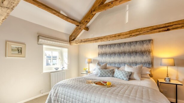 A bedroom with a large bed, wooden beams, a window with blinds, a bedside table with a lamp, and a wall-mounted artwork. - 2 Bed in Long Marton (oc-c34661) (Long Marton)