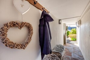 Um corredor com uma grinalda de vime em formato de coração, um porta-roupas com um casaco, um banco e vista para o exterior.