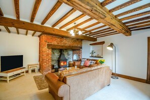 Ein Wohnzimmer mit freiliegenden Holzbalken, einem Kamin aus Ziegelsteinen, einem Ledersofa und einem Fernseher.
