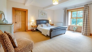 Ein Schlafzimmer mit einem Bett, Nachttischen, einem Sessel, einem Fenster mit Vorhängen und einer Tür.