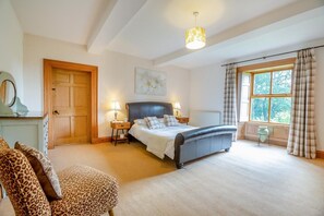 Ein Schlafzimmer mit einem Bett, Nachttischen, einem Sessel, einem Fenster mit Vorhängen und einer Tür.