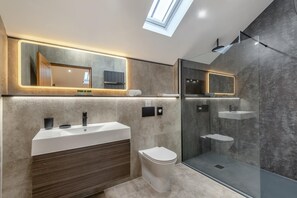 Ein modernes Badezimmer mit Dachfenster, einem großen Spiegel, einem Waschtisch und einer Duschkabine.
