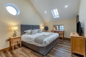 A bedroom with a bed, bedside tables, a desk, a TV, a skylight, and a fan.