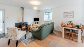 A living room with a sofa, a chair, a table with breakfast, a TV, and a fireplace. - 2 Bed in Berrynarbor (oc-l34468) (Berrynarbor)