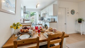 A modern kitchen with white cabinets, a dining table set with breakfast items, and a view of the outdoors. - 2 Bed in Berrynarbor (oc-l34468) (Berrynarbor)