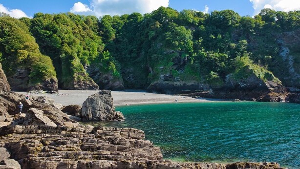 A coastal landscape with rocky formations, a sandy beach, and dense green foliage. - 2 Bed in Berrynarbor (oc-l34468) (Berrynarbor)