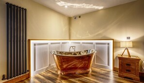 Una habitación con bañera independiente, un radiador, un armario de madera y una lámpara.