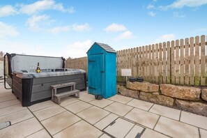Un jacuzzi, un cobertizo azul y una valla de madera en un patio trasero.