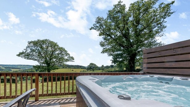 Een hottub op een houten terras met uitzicht op glooiende heuvels en bomen.