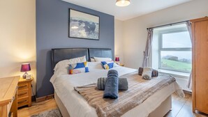 Quarto com uma cama grande, luminárias de cabeceira, janela com vista para o campo e um quadro na parede.