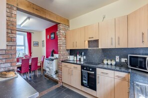 A compact kitchen with wooden cabinets, a black countertop, and a microwave. - 4 Bed in Aberystwyth (oc-374994) (Tal-y-bont)