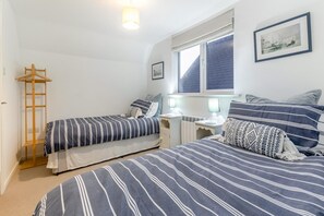 Ein Schlafzimmer mit zwei Betten, einer Holzleiter, einem Schreibtisch mit Stuhl und einem Fenster mit Jalousien.