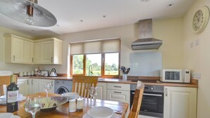 A kitchen with white cabinets, a dining table set with plates, glasses, and a bottle of wine. - 2 Bed in Llandrindod Wells (oc-510531) (Llanbister)