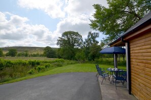 Un bâtiment en bois doté d’un patio, de sièges en plein air et offrant une vue sur la campagne.