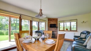 A dining area with a wooden table, chairs, and a brick fireplace. - 2 Bed in Llandrindod Wells (oc-510531) (Llanbister)