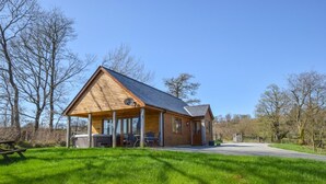 A wooden cabin with a covered porch, a picnic table, and a grill area. - 2 Bed in Llandrindod Wells (oc-510531) (Llanbister)