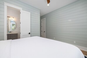 A bedroom with a bed, a vanity with a mirror, and a door leading to another room. - Stay @ Isle of Coladas (Isle of Palms)
