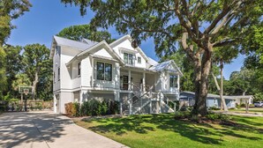 A two-story house with a front porch, a basketball hoop, and a large tree in the yard. - Stay @ Isle of Coladas (Isle of Palms)