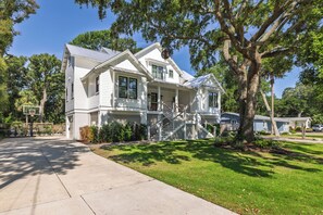 A two-story house with a front porch, a basketball hoop, and a large tree in the yard. - Stay @ Isle of Coladas (Isle of Palms)